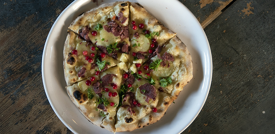 Uppskuren pizza toppad med kött, lingon och svensk ost.
